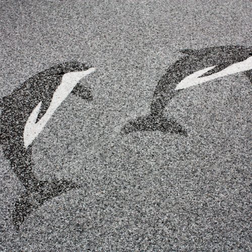 Terrasse mit Steinteppich in den Farben grau und nebelgrau. Im Boden zwei springende Delphine.