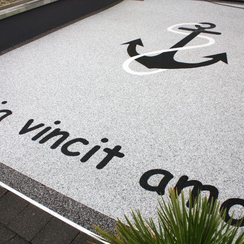 Eine, mit Steinteppich belegte Garagenzufahrt, mit einem eingearbeiteten Motiv eines Ankers und dem Schriftzug: "Omnia vincit amor".