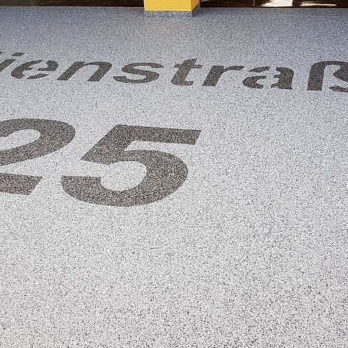 Garagenzufahrt mit Natursteinteppich und dem Straßennamen mit Steinteppich gestaltet