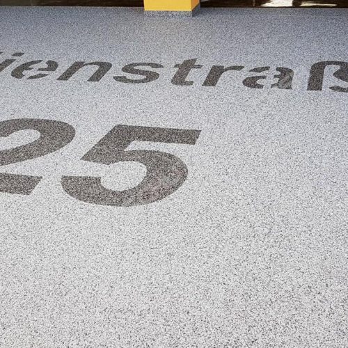 Garagenzufahrt mit Natursteinteppich und dem Straßennamen mit Steinteppich gestaltet